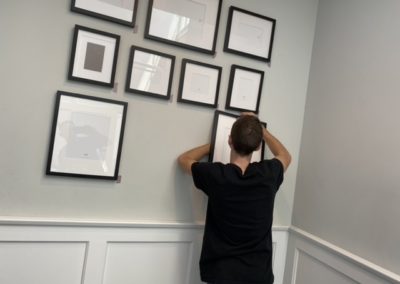Assistant hanging frames for gallery wall of photos in Manhattan Beach home